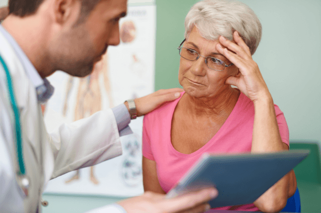 Woman in her late 50s in a doctor's office looking unconvinced, representing the experience of being told brain fog is a normal part of aging when it may have other causes.