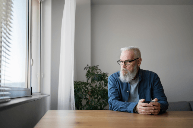 Man in his 50s staring out a window at his home office desk, illustrating the daily experience of brain fog and slipping thoughts that affect cognitive clarity over 40.