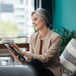 A sophisticated woman in her 60s looking at a digital tablet with a focused, sharp expression in a high-end, sunlit home library, symbolizing cognitive longevity.