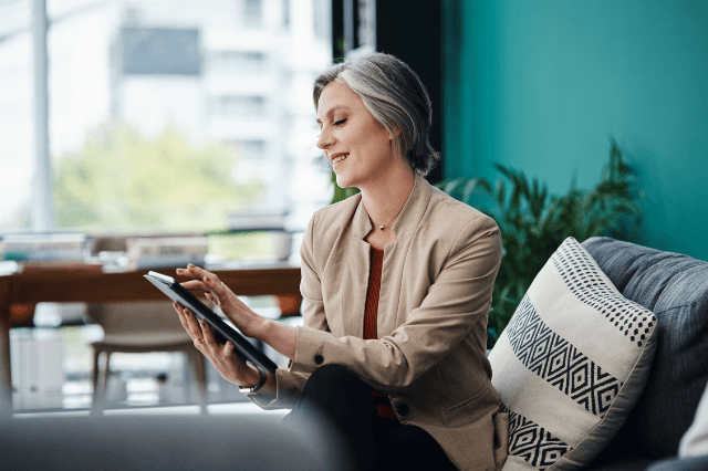 A sophisticated woman in her 60s looking at a digital tablet with a focused, sharp expression in a high-end, sunlit home library, symbolizing cognitive longevity.