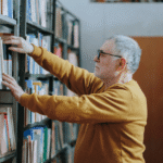 A man in his early 60s looking at a bookshelf with a calm, analytical expression, illustrating a healthy cognitive state during normal aging.